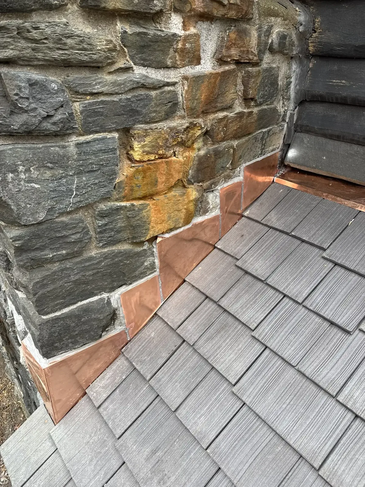 Copper flashing beside a stone chimney and slate roof