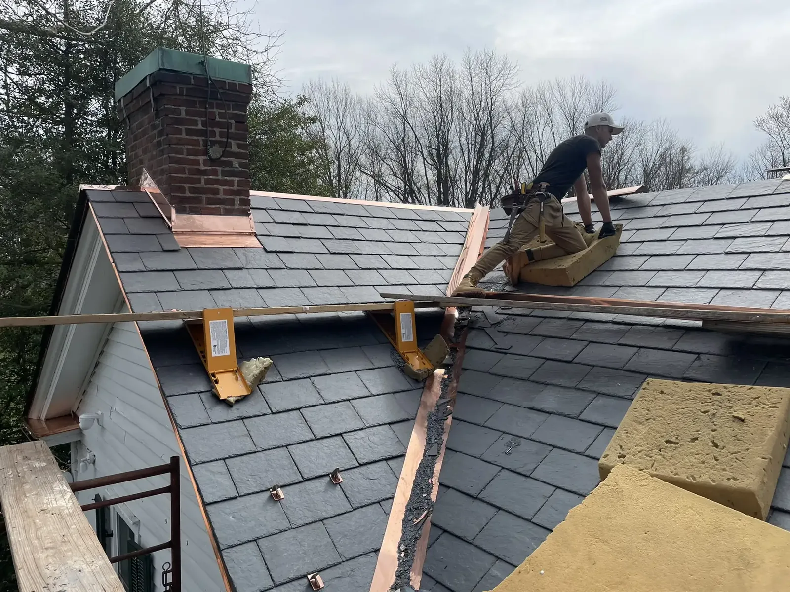 Worker installing slate roofing with copper flashing